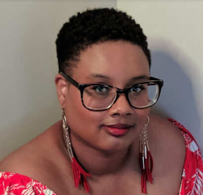 Poet Diamond Forde in a red dress, wearing glasses.