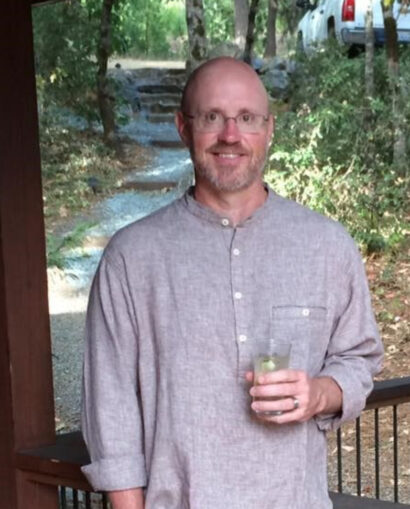 Poet Michael Rogner smiling with a glass in their hand, wearing a button down shirt