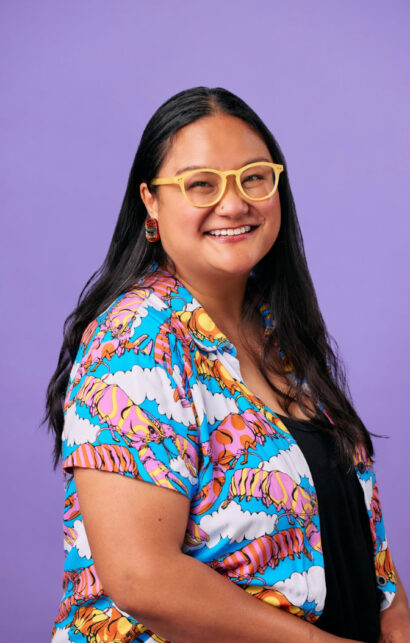 Poet Michelle Penaloza in front of a purple background smiling with yellow glasses