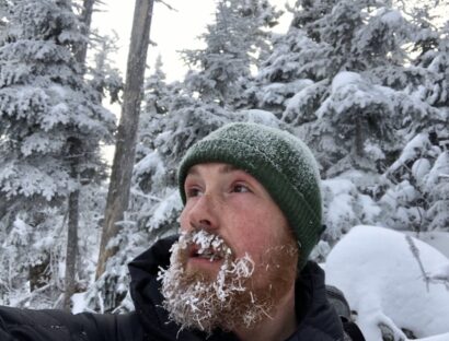 Josh in a green hat with snow in his beard, in a snowy background
