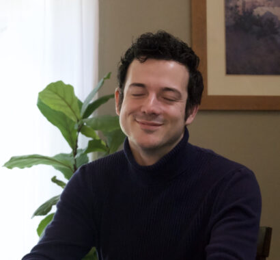 Benjamin Bartu smiling in a black shirt with a green plant behind him.