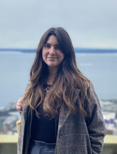 Writer Gabriella with long brown hair in a gray jacket in front of a water view