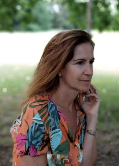 Carolina with long hair in a field, wearing a tropical patterned shirt