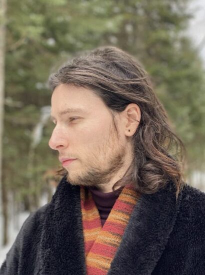 John with long brown hair in a striped red/orange scarf