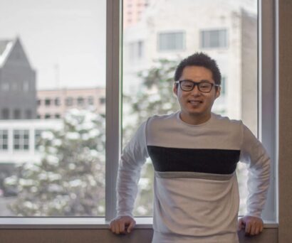 Nik in glasses with black hair smiling in front of a window