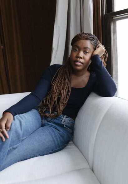 Claudia with long brown hair in a blue shirt and jeans, sitting on a couch