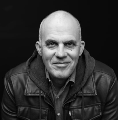 In a black and white image, Jeffrey Utzinger looks directly into the camera against a black backdrop.
