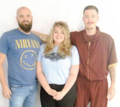 DT Holt (right) stands with two family members. All three smile at the camera against a white backdrop.