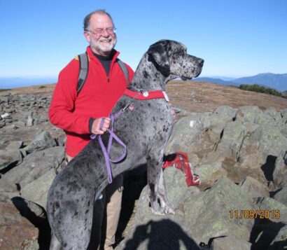 Michael Horton smiles at the camera with a rocky landscape in the background and a large, gray-spotted dog in the foreground.
