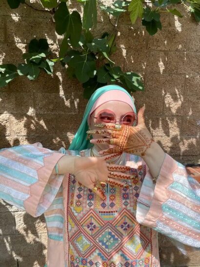 photo of author Rema Shbaita posing with hands in front of face in a striped turquoise and pink top