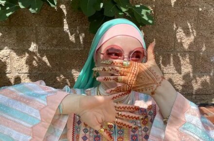 photo of author Rema Shbaita posing with hands in front of face in a striped turquoise and pink top