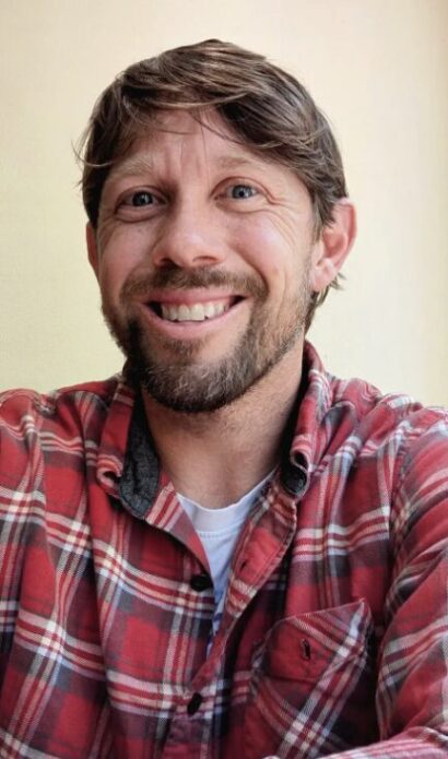 Joseph smiling with brown hair and a beard, wearing a plaid shirt