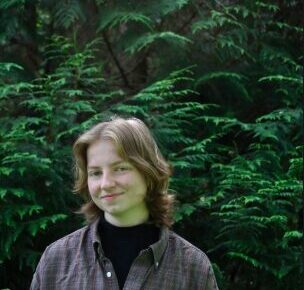 Taylar standing in a lush pacific northwestern forest in front of green ferns
