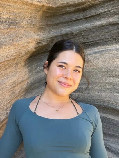 Photo of Lana Reeves with dark hair wearing a teal-colored top smiles at the camera against a backdrop of a rocky, canyon-like formation