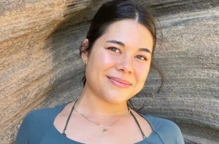 Photo of Lana Reeves with dark hair wearing a teal-colored top smiles at the camera against a backdrop of a rocky, canyon-like formation