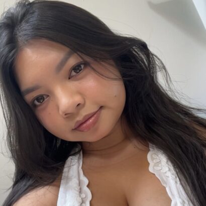 A Filipina woman with long dark hair wearing a white tank top smiles at the camera