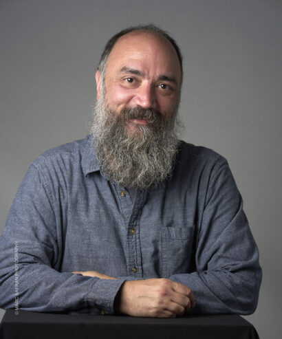 Author Christopher Citro poses for the camera, propping his forearms on a dark surface and smiling slightly for the photo