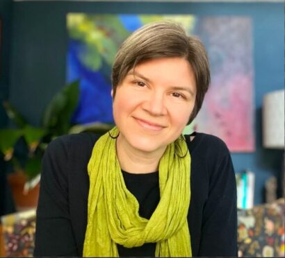 Photo of Shannon in a colorful room, smiling with a green scarf on
