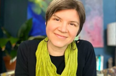 Photo of Shannon in a colorful room, smiling with a green scarf on