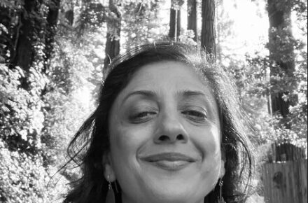 Parul Shah smiling under a canopy of trees in black and white