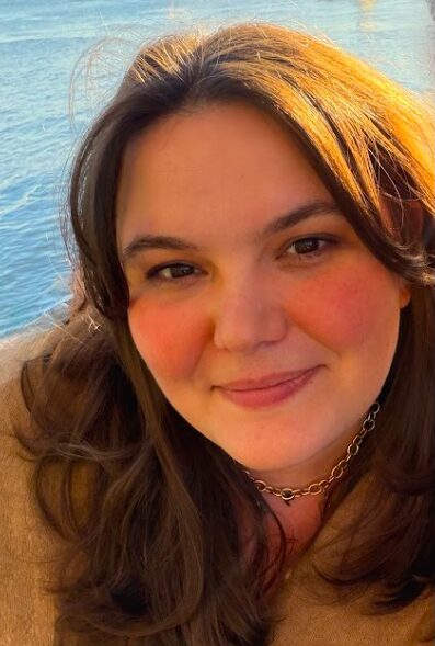 Photo of Katie in the sun, smiling near a body of water